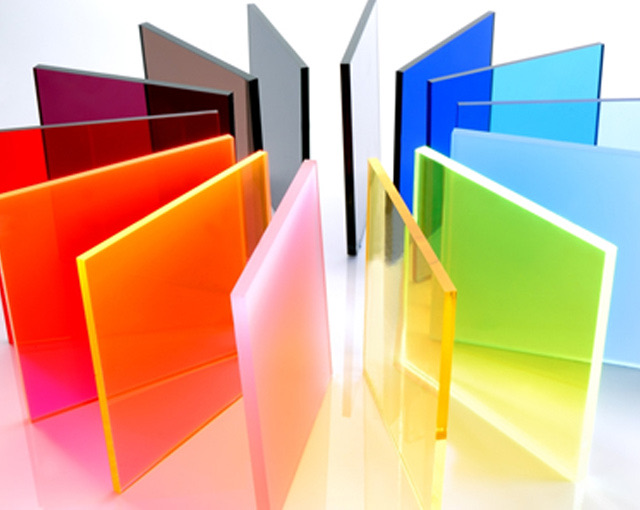 Placas de acrílico de colores: transparente, rojo, naranja, azul y verde, paradas sobre una superficie reflectante